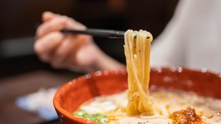 Ramen noodle lifted up by chopsticks with steam against restaurant background