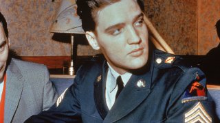Circa 1958, American singer and actor Elvis Presley (1935 - 1977) sits in a restaurant wearing his US Army uniform.