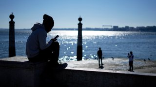 FILE - A teen checks their phone by the Tagus River on a sunny winter day, Lisbon, Portugal, Jan. 30, 2023.