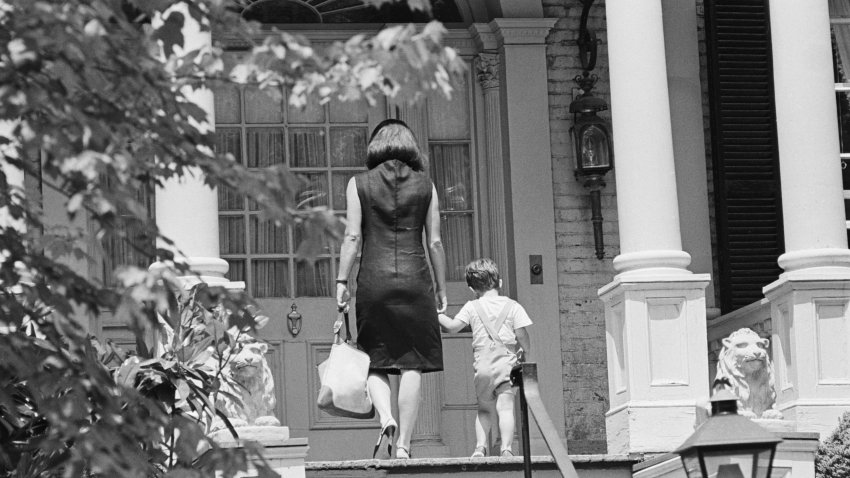 File photo of former First Lady Jackie Kennedy walking with her son John, Jr. (or “John-John”), into their Georgetown home.