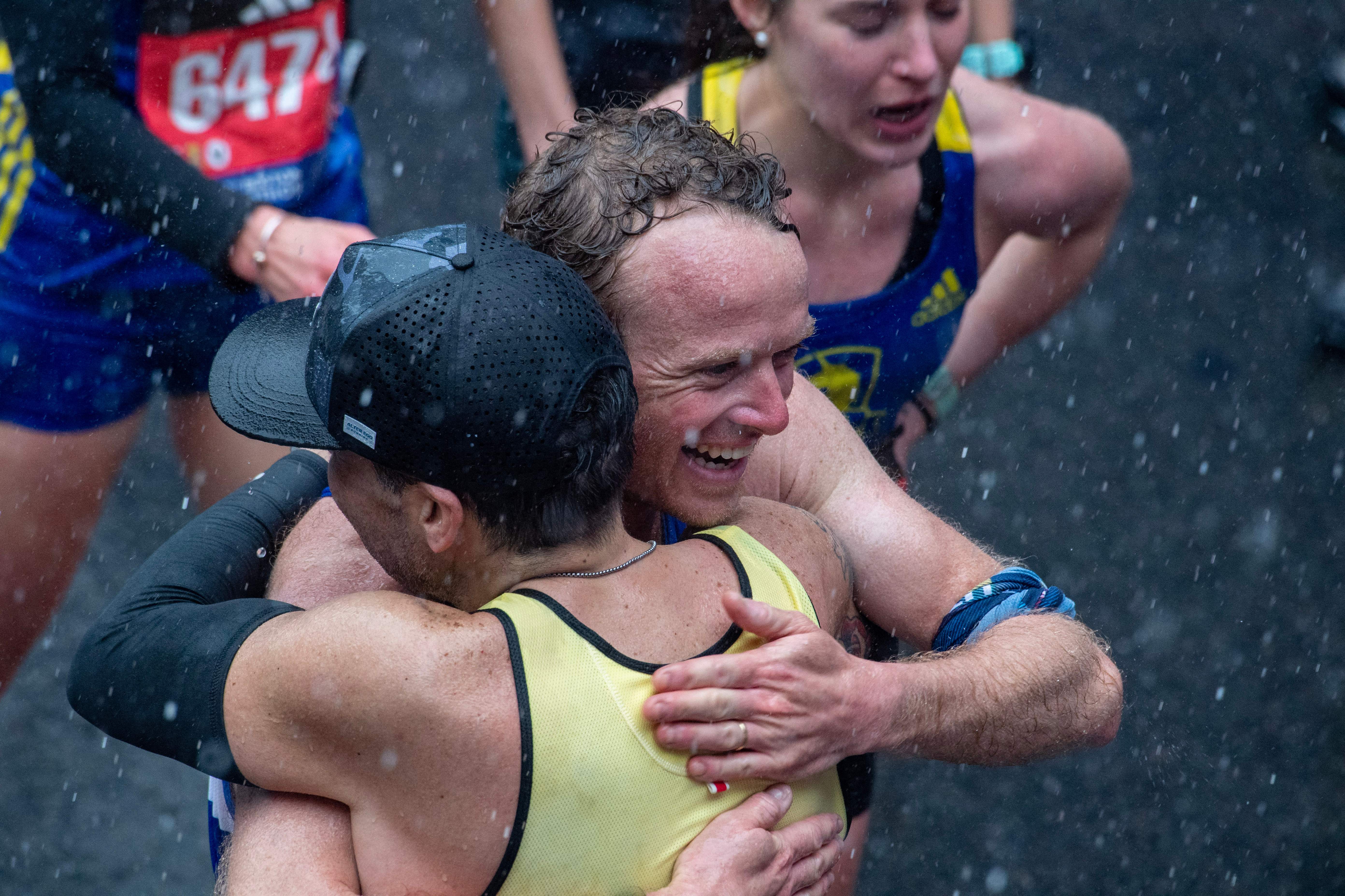 Runners embrace in the rain after finishing the race during the 127th Boston Marathon in Boston, Massachusetts on April 17, 2023. – In wet and windy conditions, 2022 champion Chebet of Kenya took his time before surging away in the closing stages to become the first man to defend the Boston crown since compatriot Robert Kipkoech Cheruiyot completed a hat trick of victories between 2006-2008. (Photo by Joseph Prezioso / AFP) (Photo by JOSEPH PREZIOSO/AFP via Getty Images)