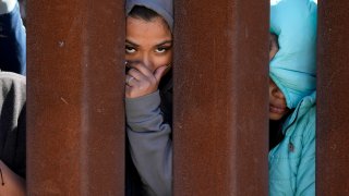 Migrants waiting to apply for asylum between two border walls look through the wall Thursday, May 11, 2023, in San Diego.