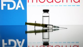 A vial and a medical syringe seen displayed in front of the U.S. Food and Drug Administration and Moderna biotechnology company’s logos.