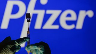 An illustrative image of a person holding a medical syringe and a vaccine vial in front of the Pfizer logo displayed on a screen.