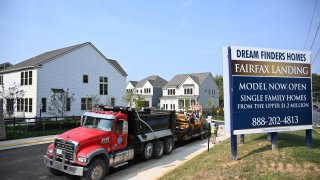 Maintenance workers in front of a housing development sign near new homes in Fairfax, Virginia, on August 22, 2023.