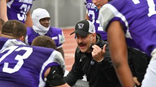 Stonehill’s football team began playing at the collegiate Division I level in 2022. As higher education becomes more competitive, some Massachusetts colleges are betting big on athletics, moving from Division 2 to Division 1 to help build up their brands and attract new students. Pictured: Offensive line coach Dylan Berardelli addresses players.