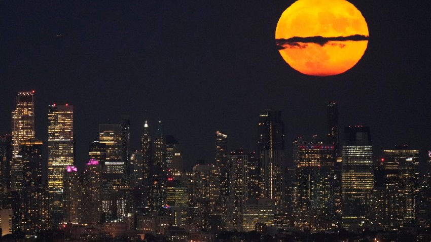 FILE – A supermoon rises through clouds over the skyline of lower Manhattan, Aug. 1, 2023, as seen from West Orange, N.J. Stargazers are in for a double treat on Wednesday night, Aug. 30: a rare blue supermoon with Saturn peeking from behind. The cosmic curtain rises Wednesday night with the second full moon of August, the reason it’s considered blue. It’s dubbed a supermoon because it’s closer to Earth than usual, appearing especially big and bright.