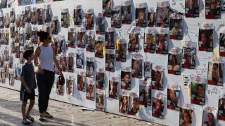 A woman with a child walks next to the wall with pictures, dedicated to hostages that are being held in Gaza after they were kidnapped from Israel by Hamas gunmen on October 7, as families and supporters of hostages hold a demonstration calling for their immediate release in Tel Aviv, Israel November 3, 2023. 