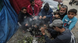 Displaced Palestinians sit in front of their tent, by a lit fire, and inspect the damage caused by rain on November 15, 2023 in Khan Yunis, Gaza. on November 15, 2023 in Khan Yunis, Gaza. Heavy fighting rages in the northern Gaza Strip as Israel encircles the area, despite increasingly pressing calls for a ceasefire. Due to a lack of fuel needed to operate the generators, hospitals are deprived of electricity. Between 15,000 and 20,000 people took shelter in hospital facilities, according to the health ministry in the Hamas-run Gaza Strip. The WHO considers “the situation disastrous and perilous”. (Photo by Ahmad Hasaballah/Getty Images)