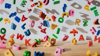 Conceptual image of colourful falling letters, casting shadows on a white wall.