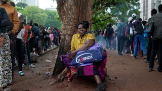 A woman takes a break from the queue outside the passport offices in Harare, Wednesday, Dec. 20, 2023. Atop many Christmas wish lists in economically troubled Zimbabwe is a travel document and people are flooding the passport office this holiday season ahead of a price hike planned in the New Year.