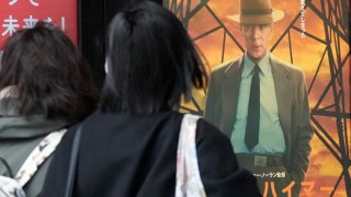 People walk in front of posters of films showing at a movie theater