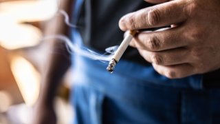 Detail of a man holding a smoking cigarette in his hand.