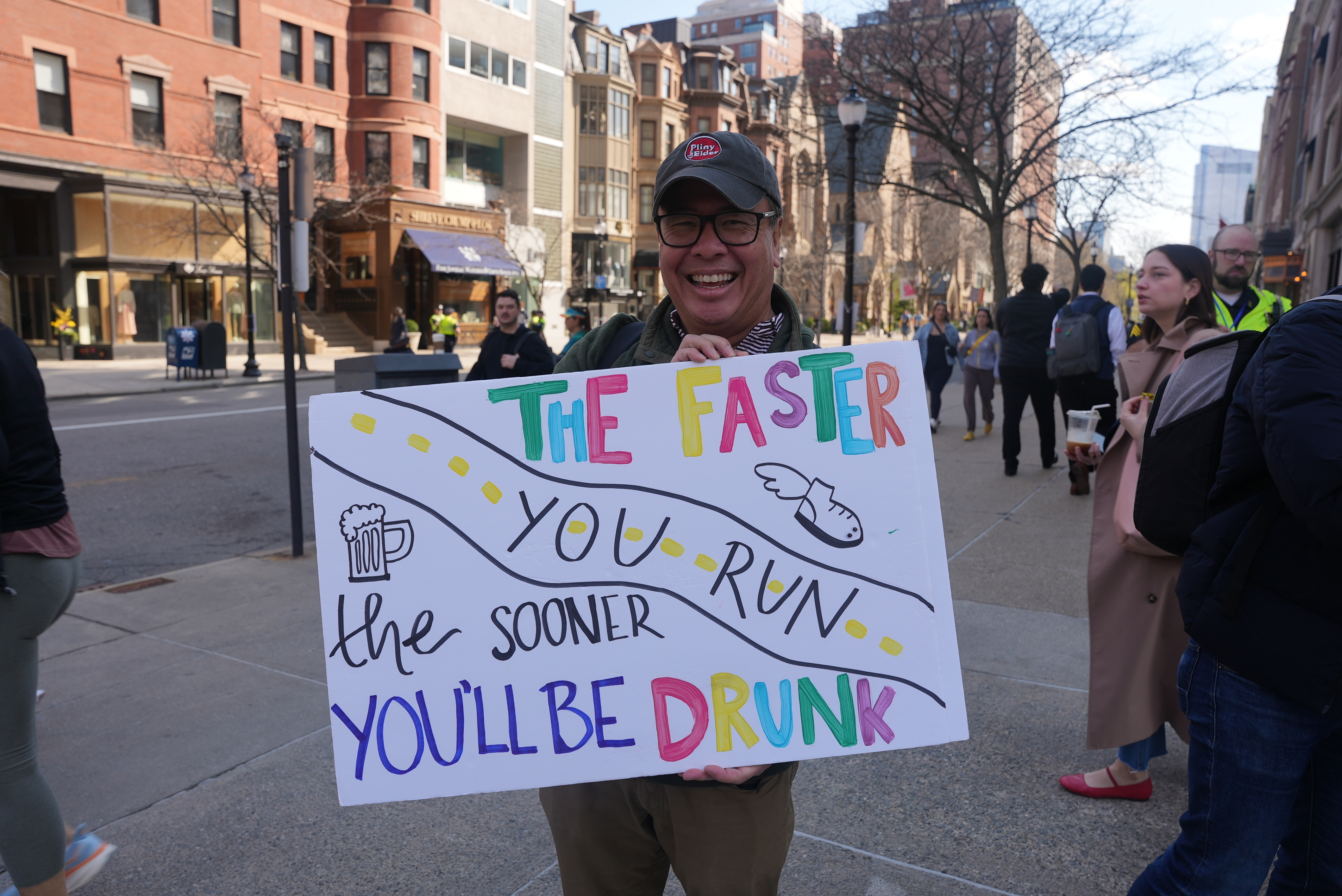 Brad Lew holding a sign saying, "The faster you run, the sooner you'll be drunk," to support his daughter, Sydney, while during the Boston Marathon on Monday, April 15, 2024. 