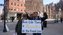 Brad Lew, left, and his daughter's boyfriend hold signs supporting the woman, who was running the Boston Marathon on Monday, April 15, 2024. One says, "Run like there's a Felipe's marg at the finish line," the other says, "Syd's faster than a sandworm on spice."