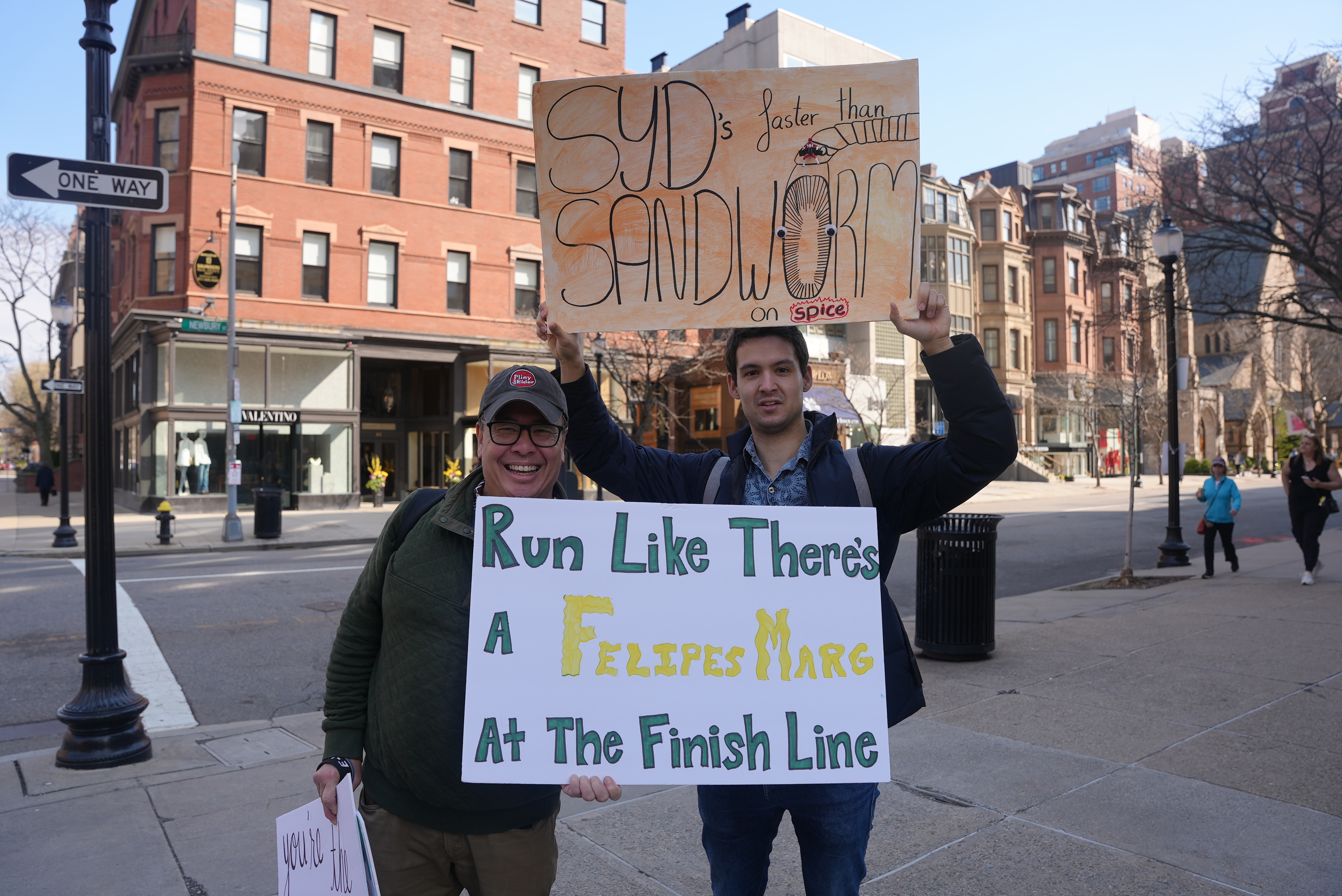 Brad Lew, left, and his daughter's boyfriend hold signs supporting the woman, who was running the Boston Marathon on Monday, April 15, 2024. One says, "Run like there's a Felipe's marg at the finish line," the other says, "Syd's faster than a sandworm on spice."