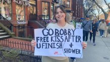 A woman on Newbury Street holds a Boston Marathon support sign that reads, "Go Bobby. Free kiss after U finish (+ shower)"