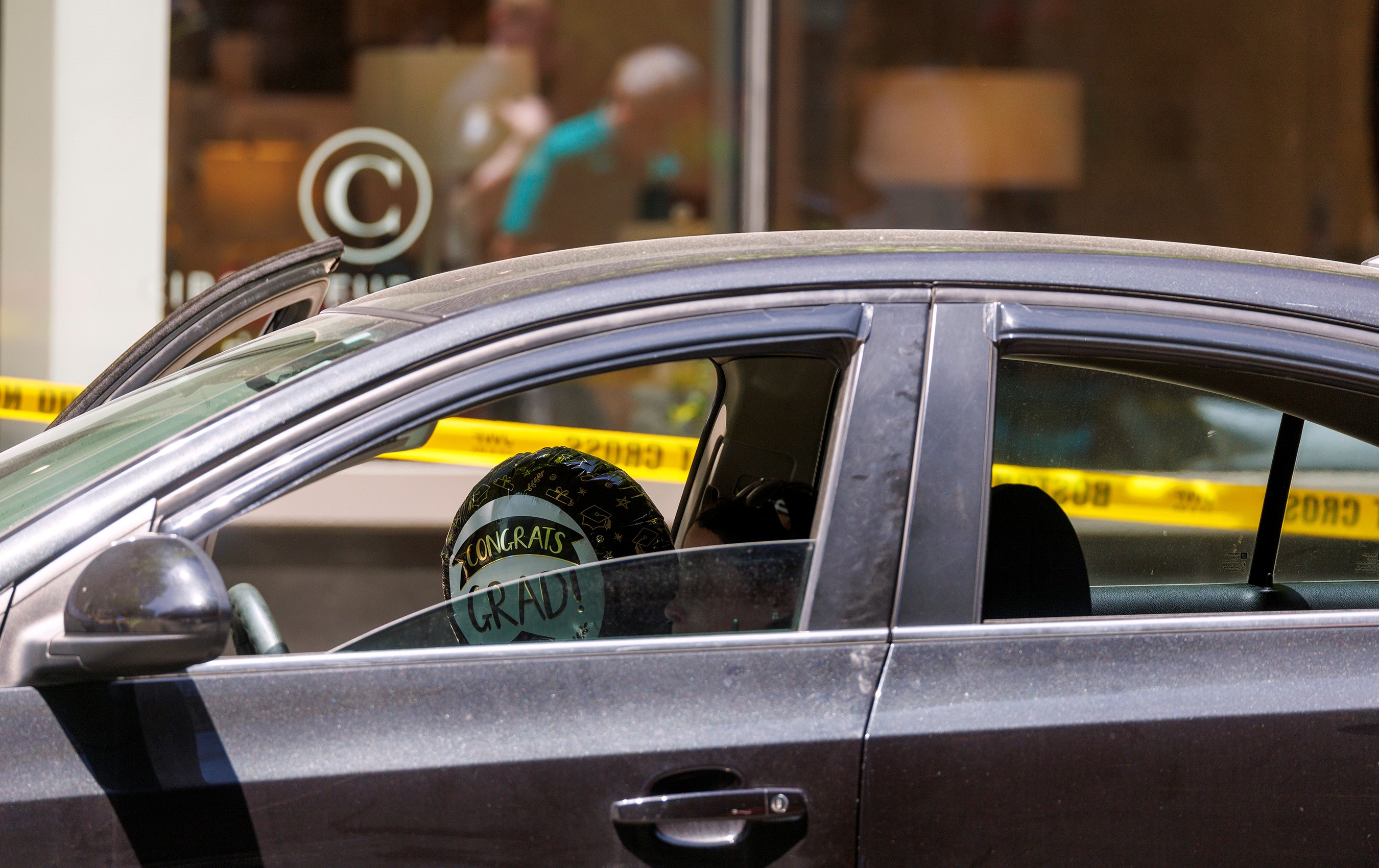 A balloon that reads, "Congrats grad!" in a car that's surrounded by police tape in Boston's Seaport District after a shooting Thursday, June 13, 2024. An 18-year-old woman who'd attended her high school nearby was wounded, police said.