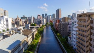 A block of industrial factories sits among newer apartment buildings along a canal in Tokyo, Japan. 