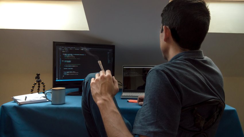 A young man smokes a joint and drinks coffee at home while working.