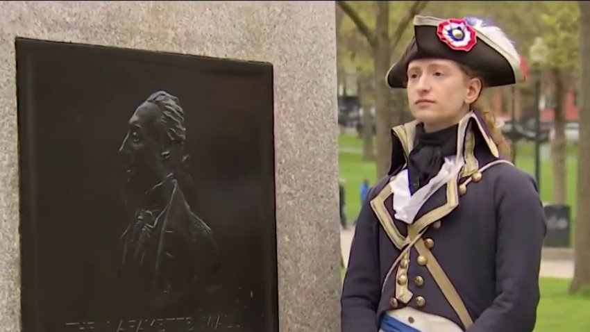 A tour guide on Boston's Freedom Trail dressed up as the Marquis de Lafayette, standing next to a plaque commemorating the Revolutionary War hero.