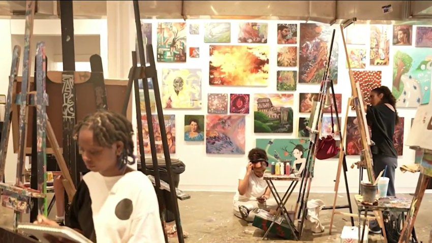 Teen artists sit at easels in a space surrounded by wall art