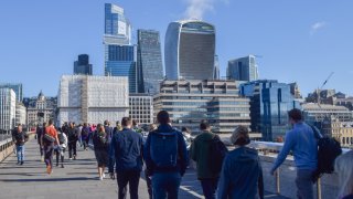 People walk along London Bridge past the City of London skyline.