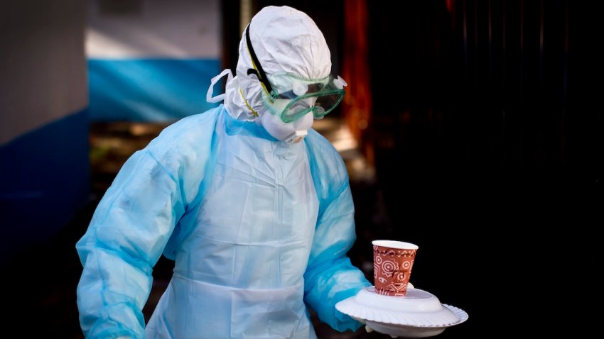 a medical worker from the Infection Prevention and Control unit wearing full protective equipment carries a meal to an isolation tent housing a man being quarantined after coming into contact in Uganda with a carrier of the Marburg Virus.