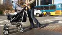 Young woman pushing baby stroller on urban sidewalk, low section