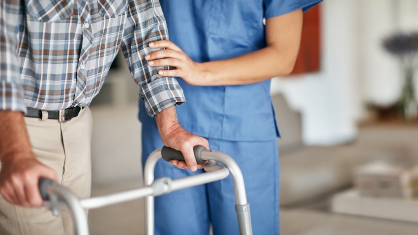 Shot of a woman assisting her elderly patient who’s using a walker for support