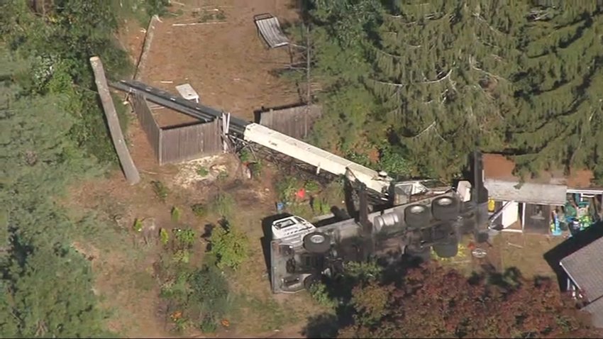 A crane on its side surrounded by trees, a fence and other wooden structures.