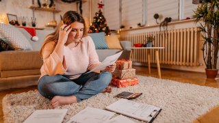 Worried woman manage bills paying at home. Sitting on floor, Christmas decorations all around the room.