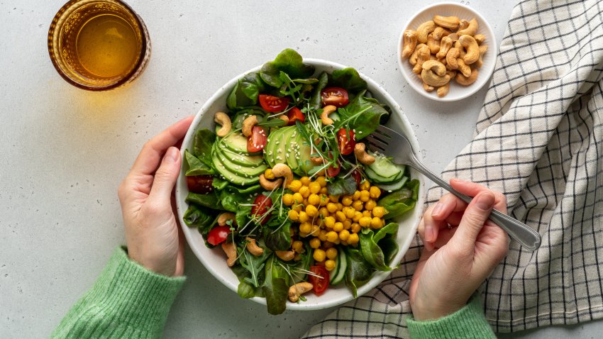 Anonymous female dining healthy vegan plant-based salad in bowl with avocado, cashew, micro-greens, pok choi, chickpeas, tomato, lettuce, cucumber, sesame