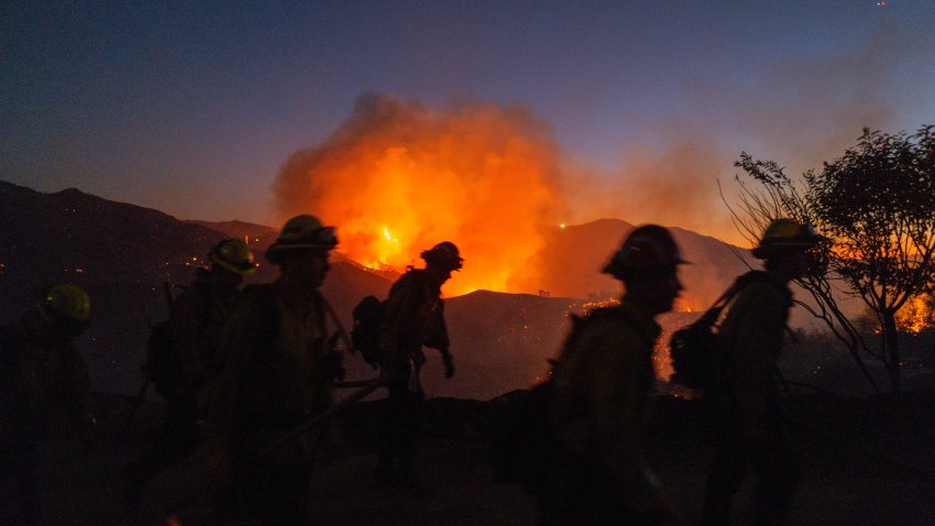 Firefighters work while smoke rises because of the growing Palisades fire in Los Angeles, California, on January 11, 2025.