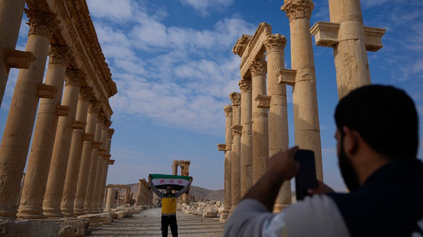 A member of the Syrian Civil Defense (White Helmets) takes a photo of his colleague holding the new Syrian flag at the ancient city of Palmyra, Syria, Saturday, Jan. 25, 2025.