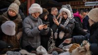 A woman, right, looks at herself on her phone as she and others buy warm winter hats at a vendors shop in the Panjiayuan Market on December 6, 2024 in Beijing, China. 
