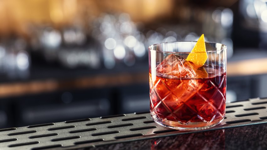 Negroni classic cocktail and gin short drink with sweet vermouth, red bitter liqueur and dried orange peel on bar counter.