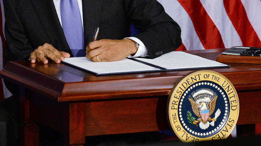 Obama's left hand signs executive order on desk with presidential seal