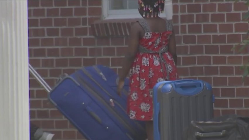 A young girl surrounded by luggage stands outside a building.