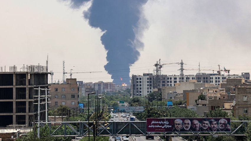 Portraits of Iranian military generals and nuclear scientists, killed in Israel’s June 13 attack are displayed above a road, as a plume of heavy smoke and fire rise over an oil refinery in southern Tehran, after it was hit in an overnight Israeli strike, on June 15, 2025.