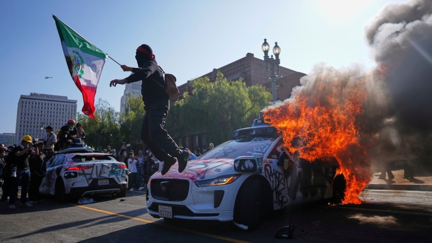 A protester leaps off a burning Waymo taxi near the Metropolitan Detention Center in downtown Los Angeles, Sunday, June 8, 2025, following last night’s immigration raid protest.