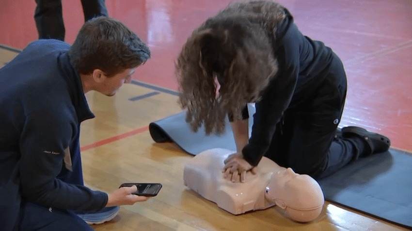 A high school student learns CPR on a dummy.