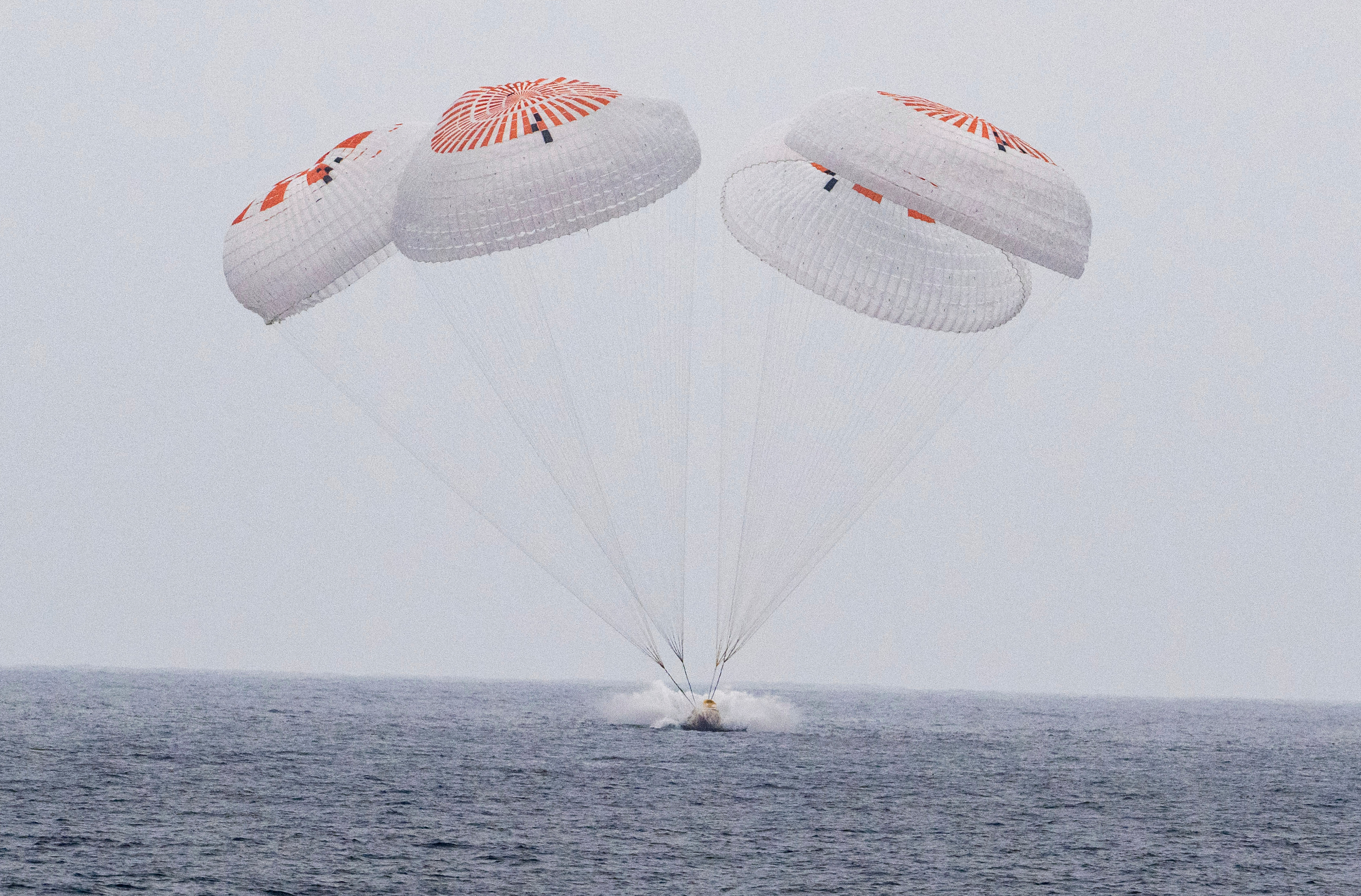 In this image provided by NASA, SpaceX capsule carrying four astronauts, parachutes into the Pacific Ocean