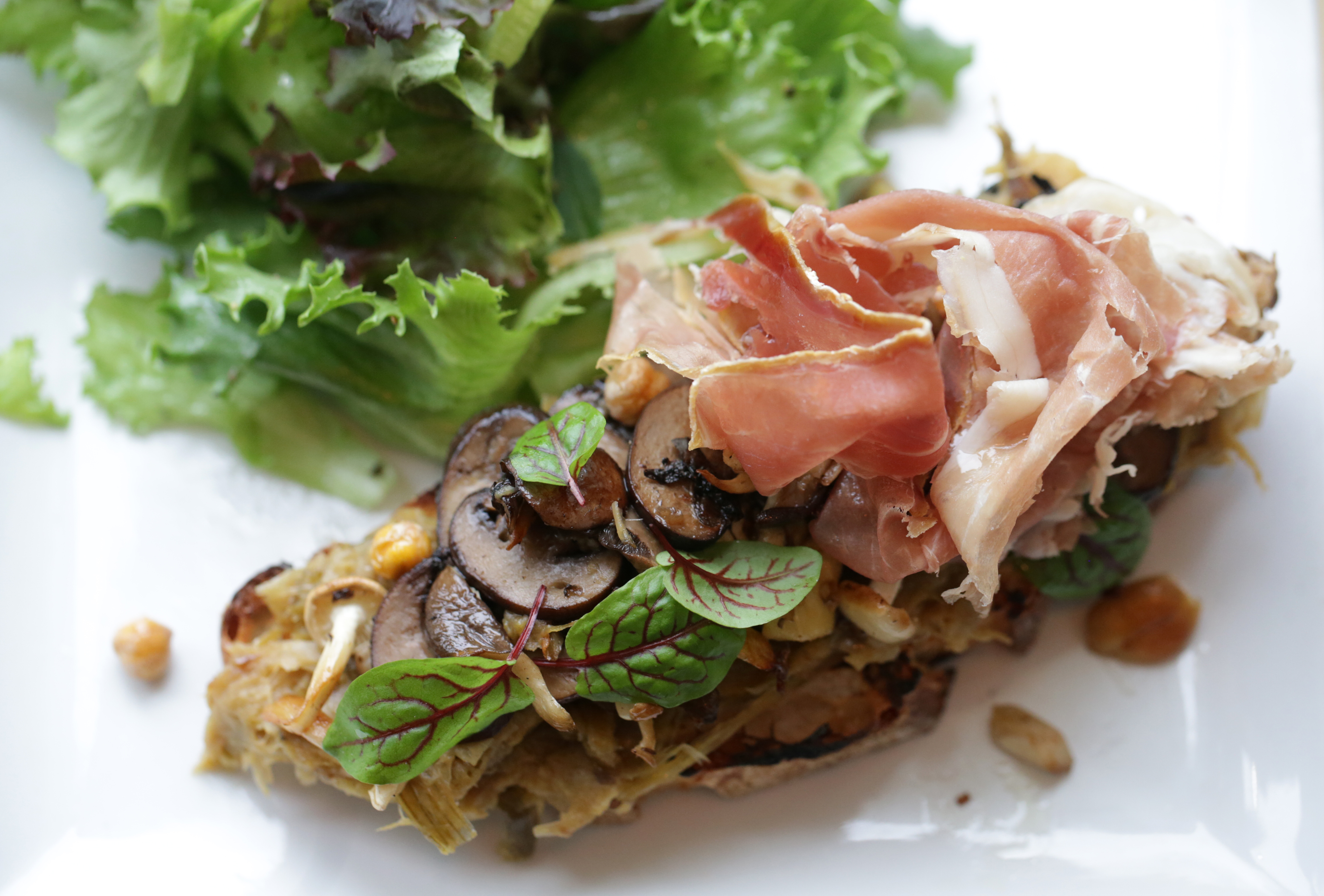 CAMBRIDGE, MA - APRIL 4: This file photo shows a tartine of roasted wild mushrooms and leek confit on grilled bread, garnished with crispy chickpeas and prosciutto and served with a field green salad at Urban Hearth in Cambridge, Massachusetts.
