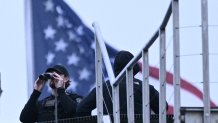 A police officer uses binoculars on the roof of a building at the White House in Washington, DC, after shots were reportedly fired on May 23, 2026. 