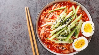 Korean spicy cold noodles Bibim Guksu closeup in the bowl on the table. Horizontal top view from above