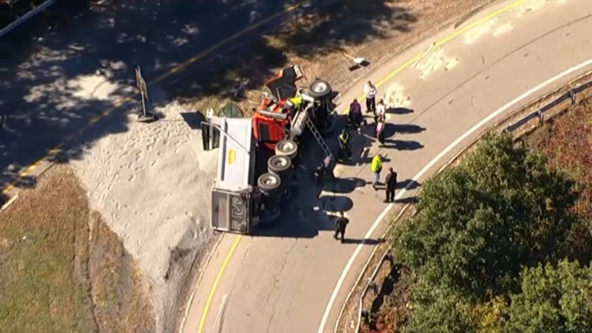 A dump truck on its side on an I-95 exit ramp in Weston, Massachusetts, on Tuesday, Oct. 6, 2026.